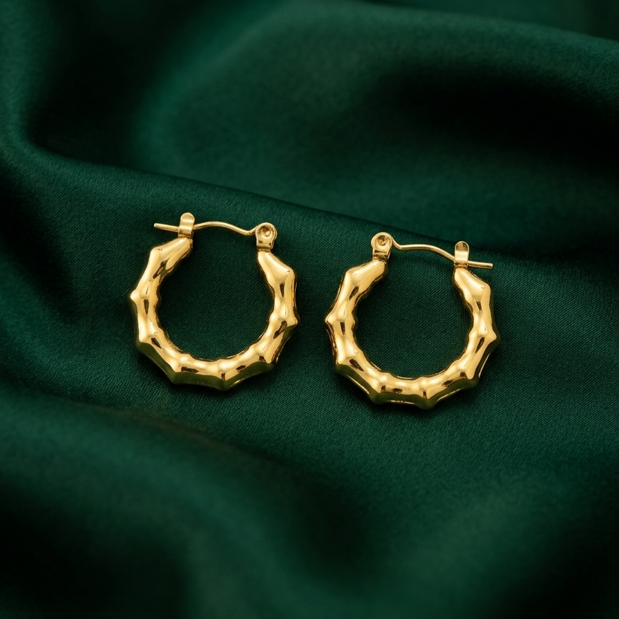 Pair of 18k gold plated mini hoop huggie earrings featuring a sculpted, textured bamboo design on a dark green fabric background