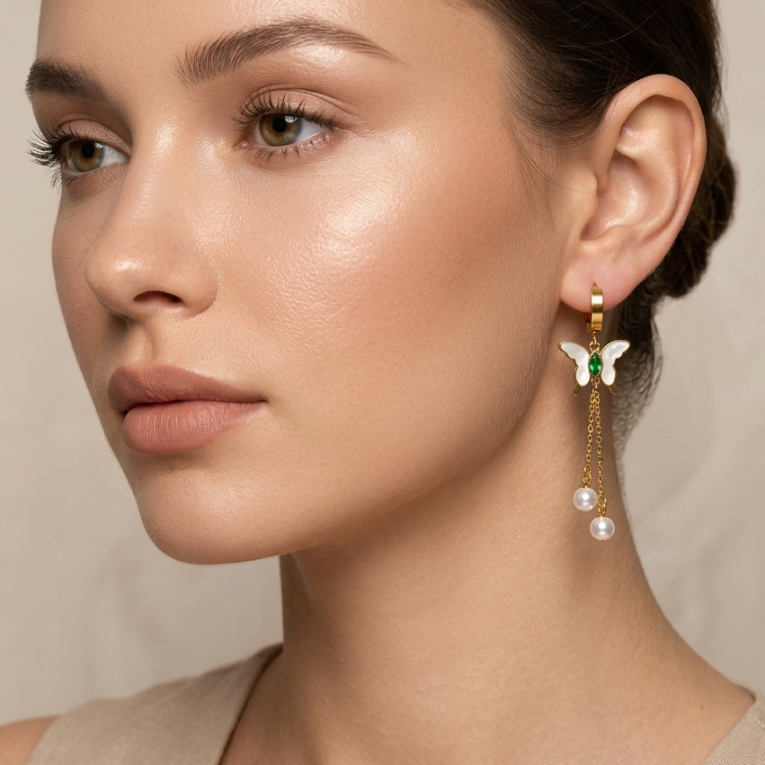 Close-up of a woman wearing butterfly pearl drops earrings with a neutral background.