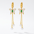 Butterfly-shaped earrings with gold frames, green gemstones, and pearl drops floating on a white background.