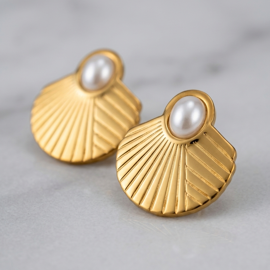 A pair of gold-toned fan-shaped earrings with a white pearl at the center, displayed on a light gray marble surface.