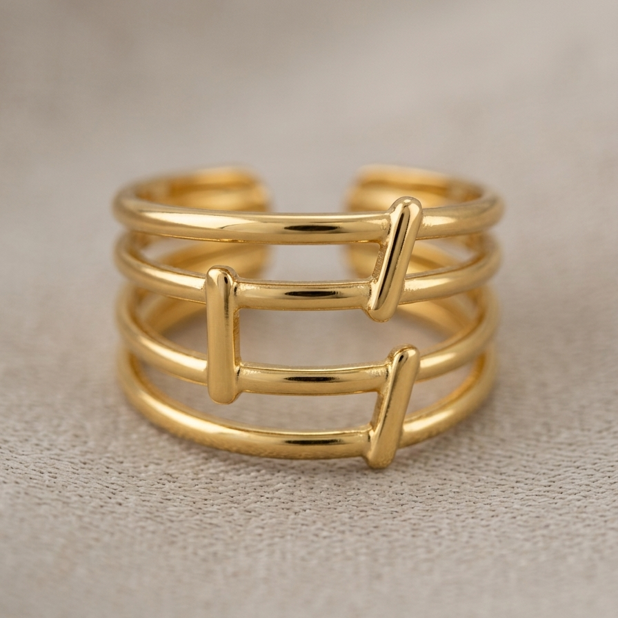 A gold-plated open bangle ring with three parallel horizontal bands and two vertical connector bars, displayed on a textured beige surface.