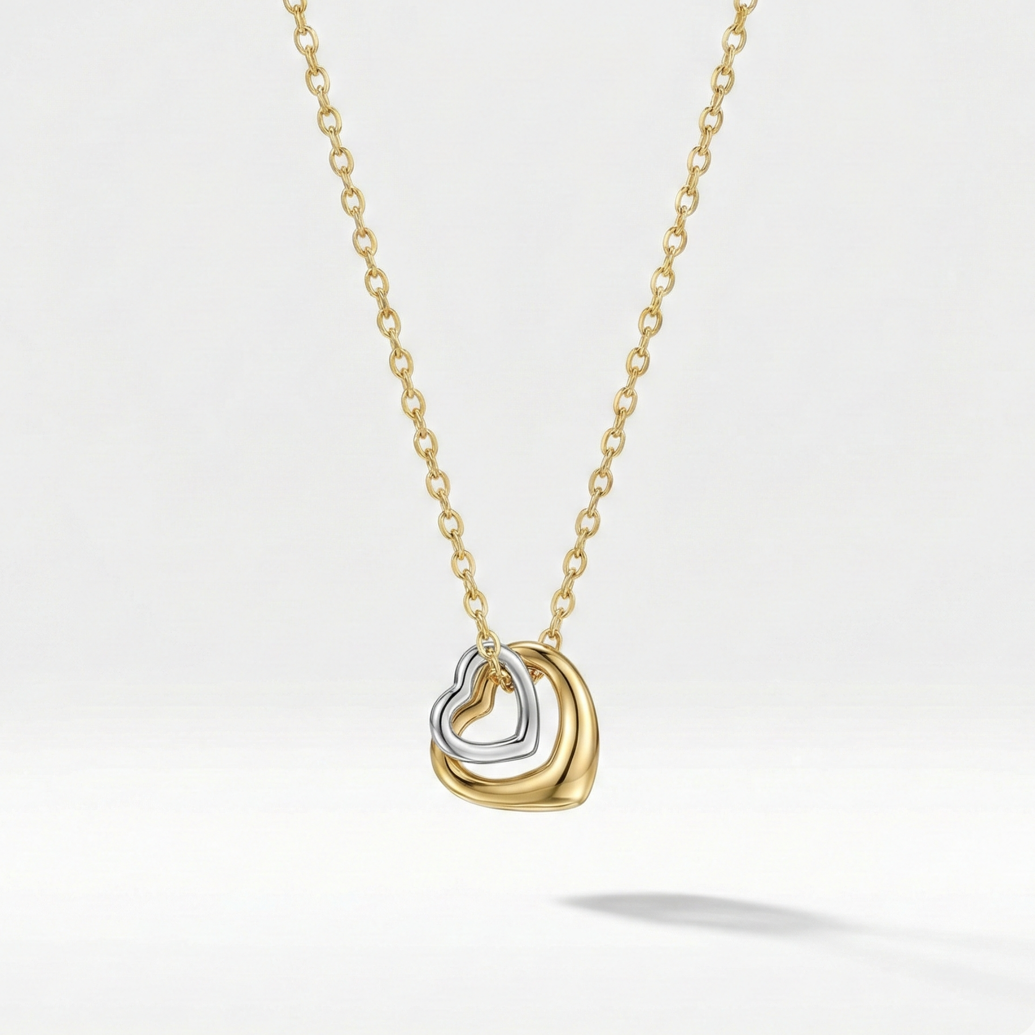 Gold necklace with double interlocking open heart pendant on beige plate.