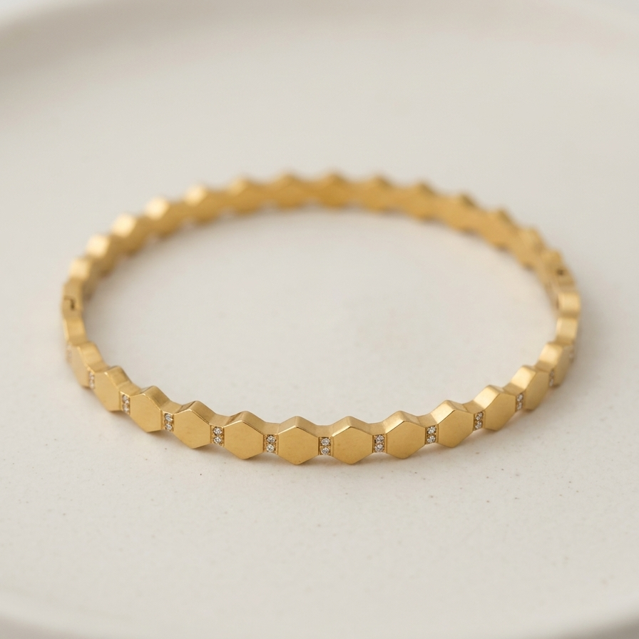 A gold-toned beaded bracelet with small clear stones between each bead, displayed on a light beige ceramic plate.