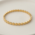 A gold-toned beaded bracelet with small clear stones between each bead, displayed on a light beige ceramic plate.