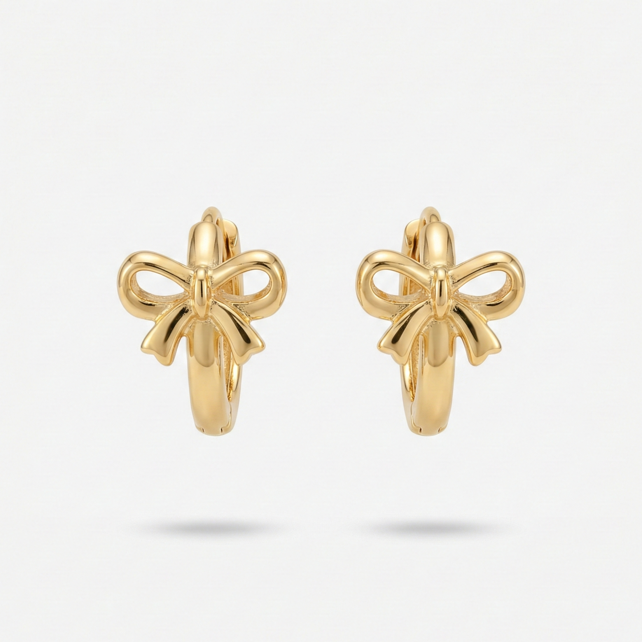 Gold ribbon bow huggie earrings on white ceramic plate.