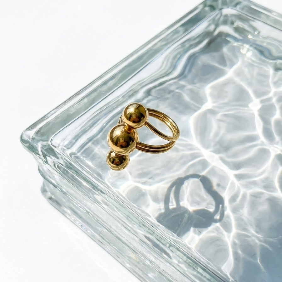 Gold ring with three polished metal balls in orbit design on white background.