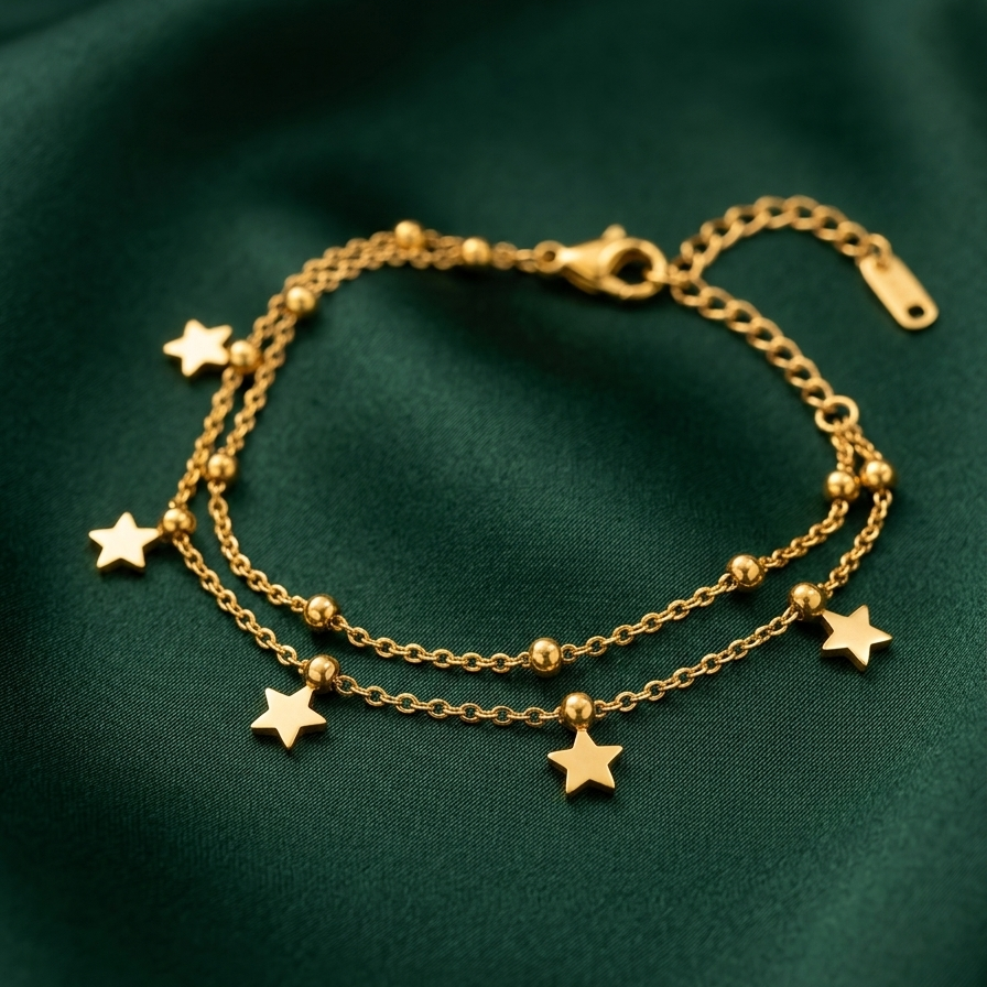 A delicate gold double-strand chain bracelet adorned with small star charms and bead accents, displayed on a dark green satin fabric background.