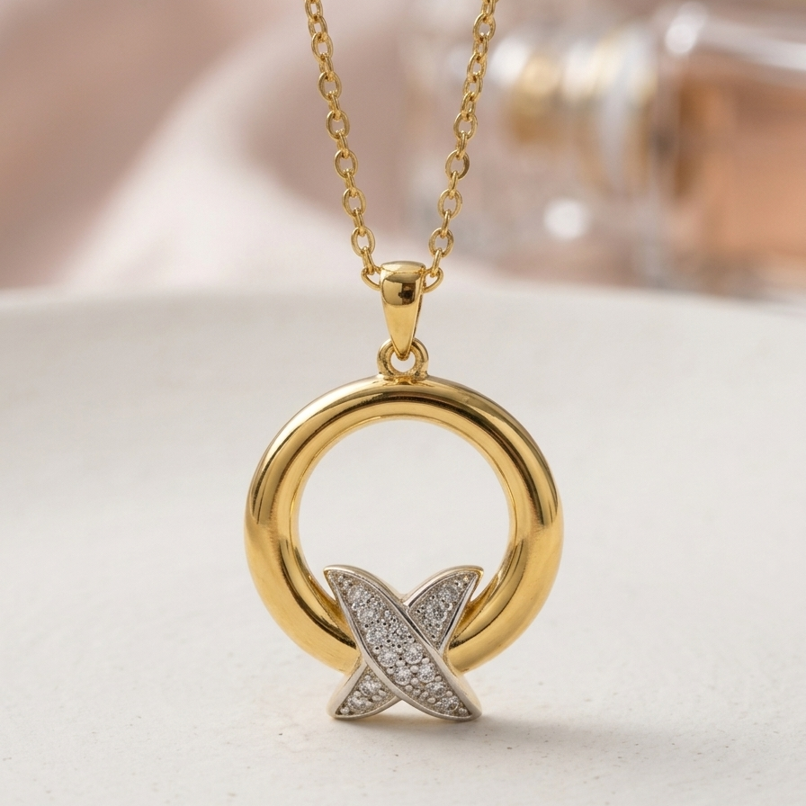 A gold pendant necklace featuring a polished circular ring with a silver-toned cross motif paved with small clear stones, hanging on a delicate gold chain against a soft beige background.