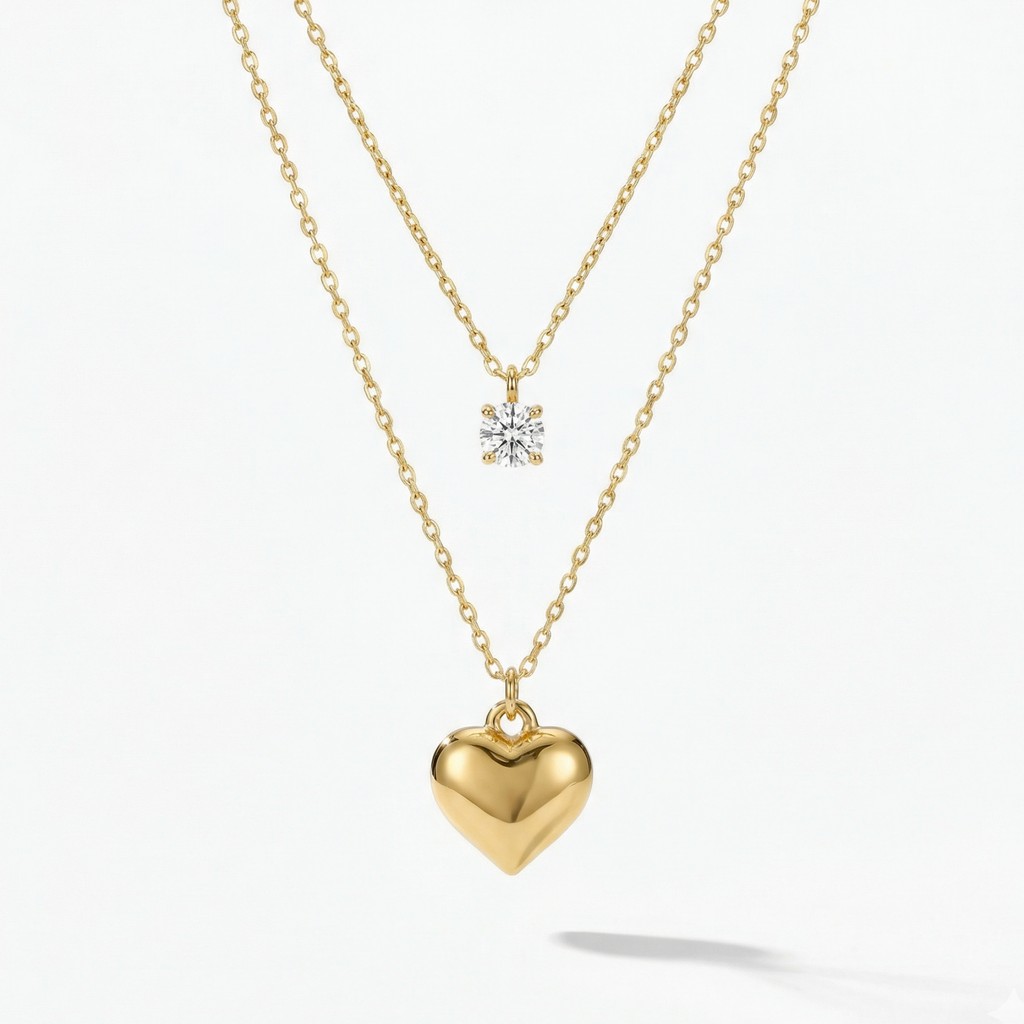 Double layered gold necklace with crystal solitaire and puffy heart pendant on beige plate.