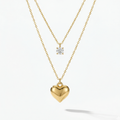 Double layered gold necklace with crystal solitaire and puffy heart pendant on beige plate.