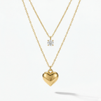 Double layered gold necklace with crystal solitaire and puffy heart pendant on beige plate.
