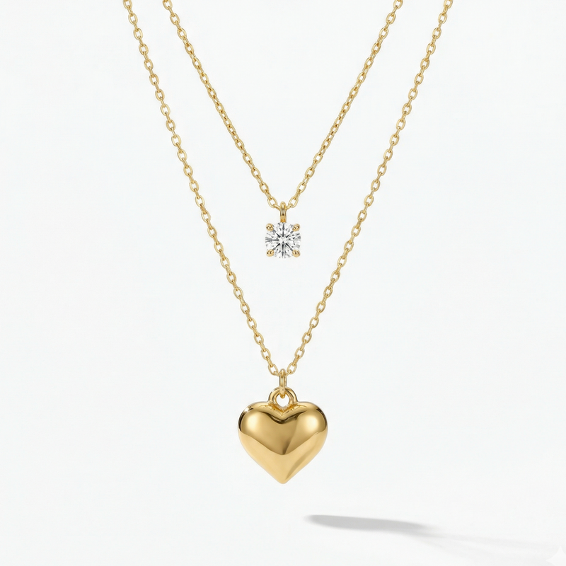 Double layered gold necklace with crystal solitaire and puffy heart pendant on beige plate.