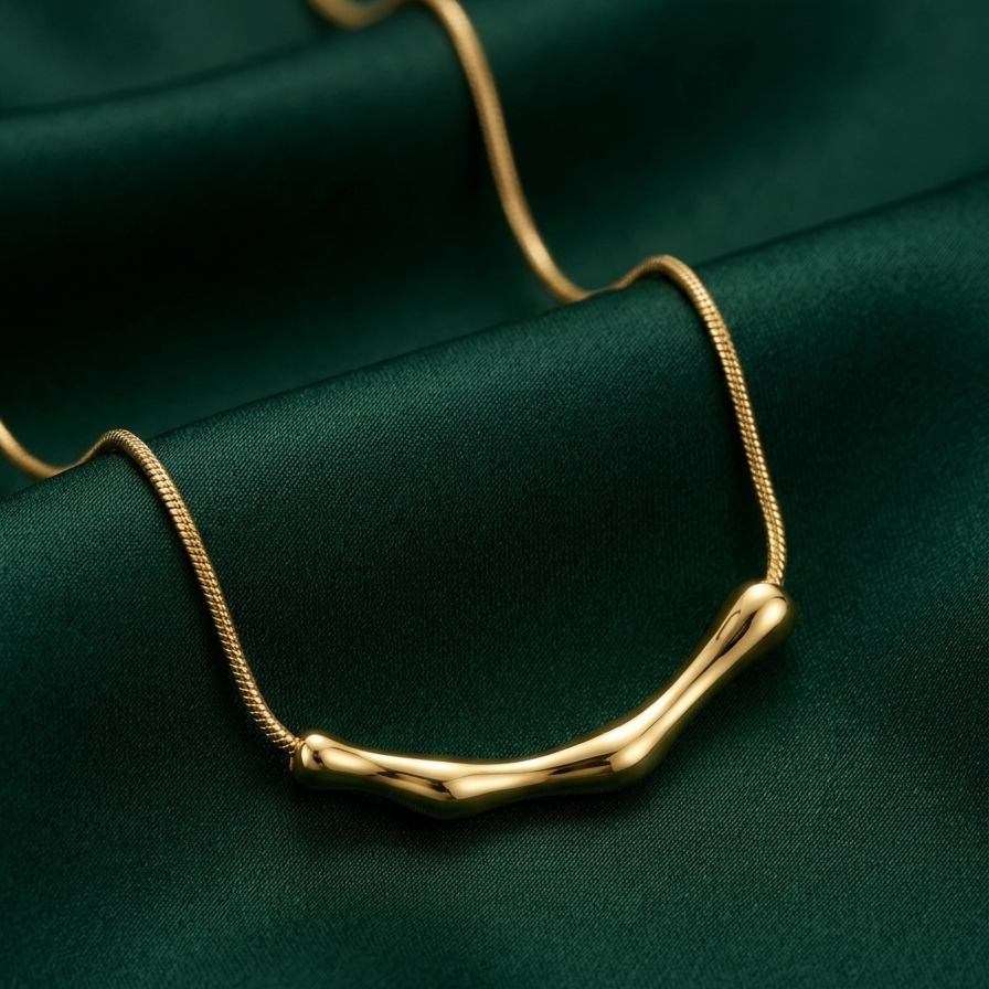 18kt gold plated bamboo bar necklace on a green fabric background.