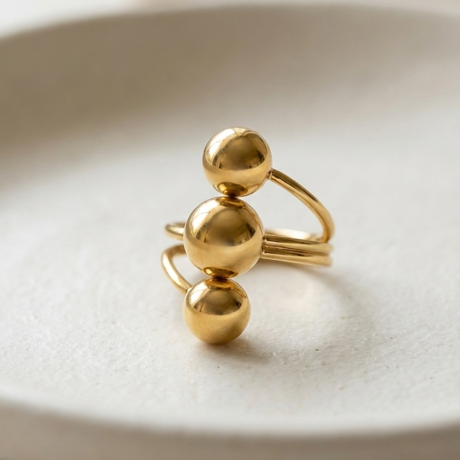 Gold ring with three polished metal balls in orbit design on white background.