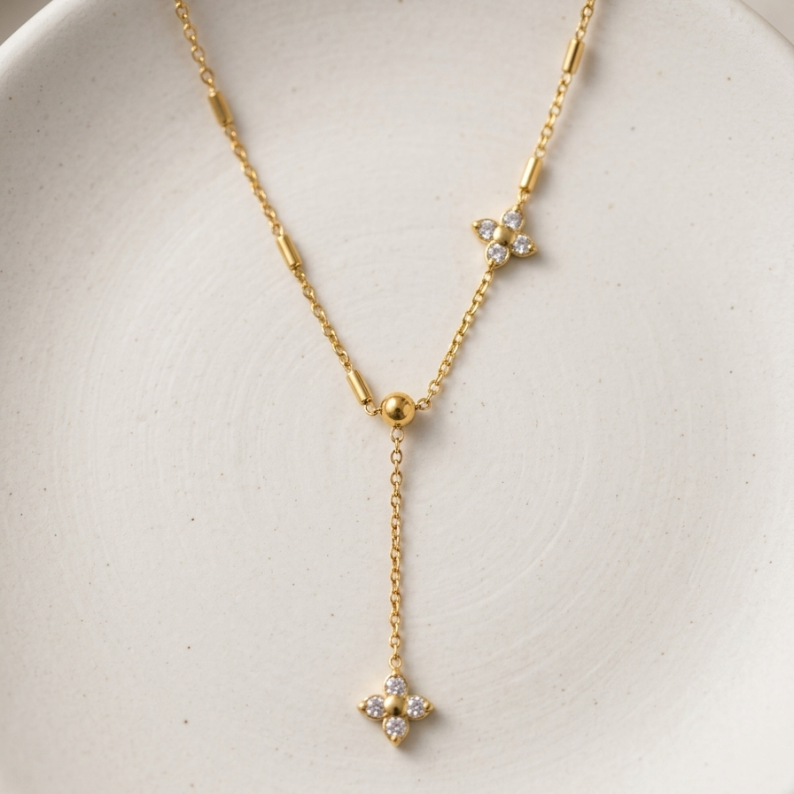 A delicate gold Y-necklace with three small floral starburst charms set with clear stones, displayed on a textured white ceramic dish.