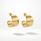 Wide sculpted gold huggie earrings on beige stone background.