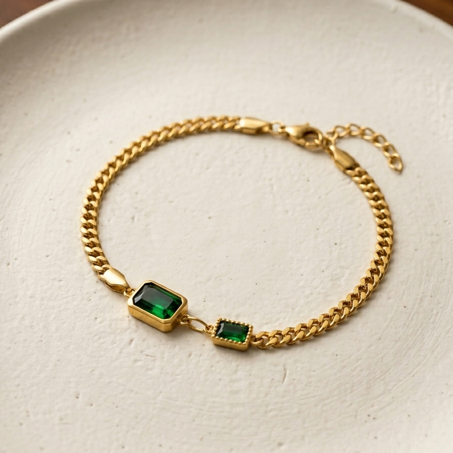 Gold bracelet with green gemstones on a white plate