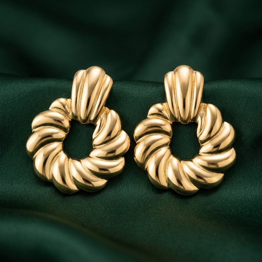 A pair of gold-toned twisted hoop earrings with a textured, ribbed design, displayed on a dark green satin fabric background.