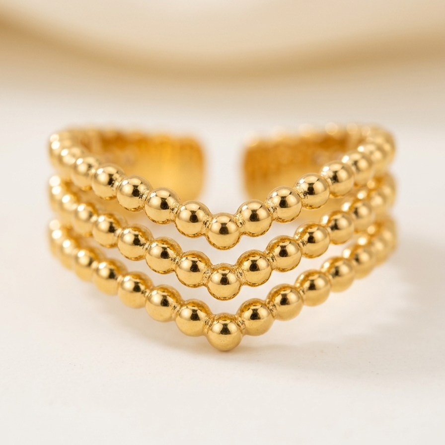 A gold-toned beaded wrap-style ring with three parallel rows of polished round beads, photographed on a soft cream background.