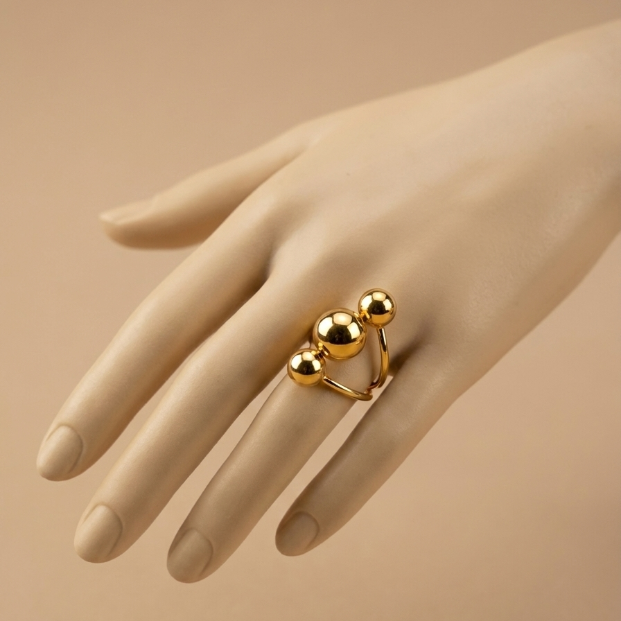 Gold ring with three polished metal balls in orbit design on white background.