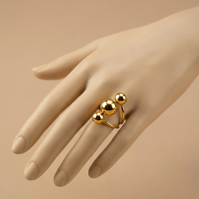 Gold ring with three polished metal balls in orbit design on white background.