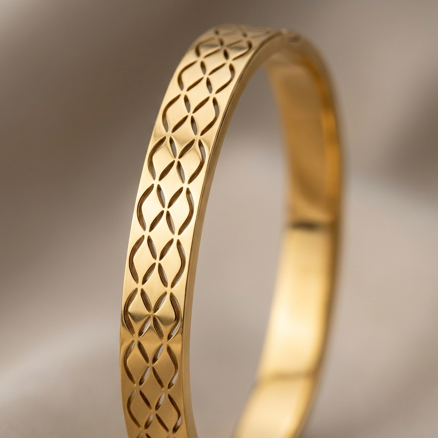A gold bangle bracelet with an intricate openwork geometric lattice pattern, shown on a neutral beige background.
