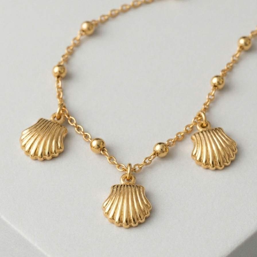 Close-up of 18kt gold plated shell charms necklace on a light gray background.