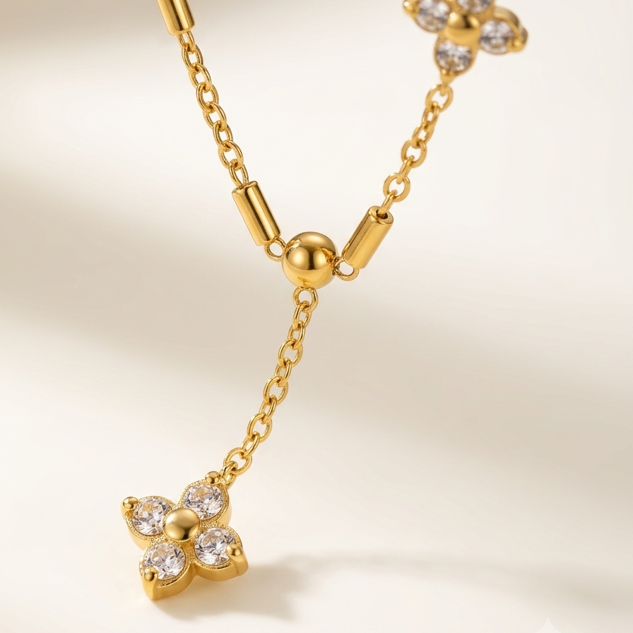 A gold Y-necklace featuring three flower-shaped motifs, some adorned with clear crystals, displayed on a soft beige background.