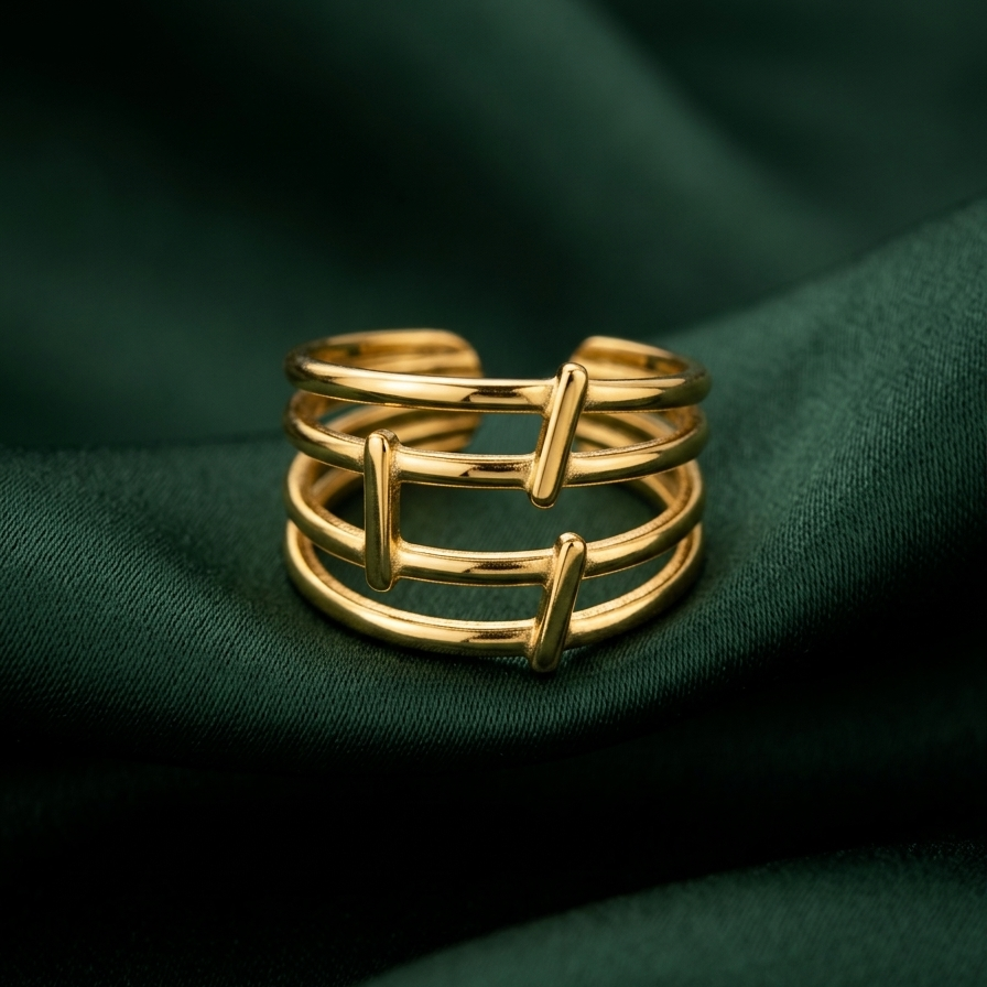 A gold-toned multi-band ring with a modern geometric twisted design, resting on draped dark green fabric.