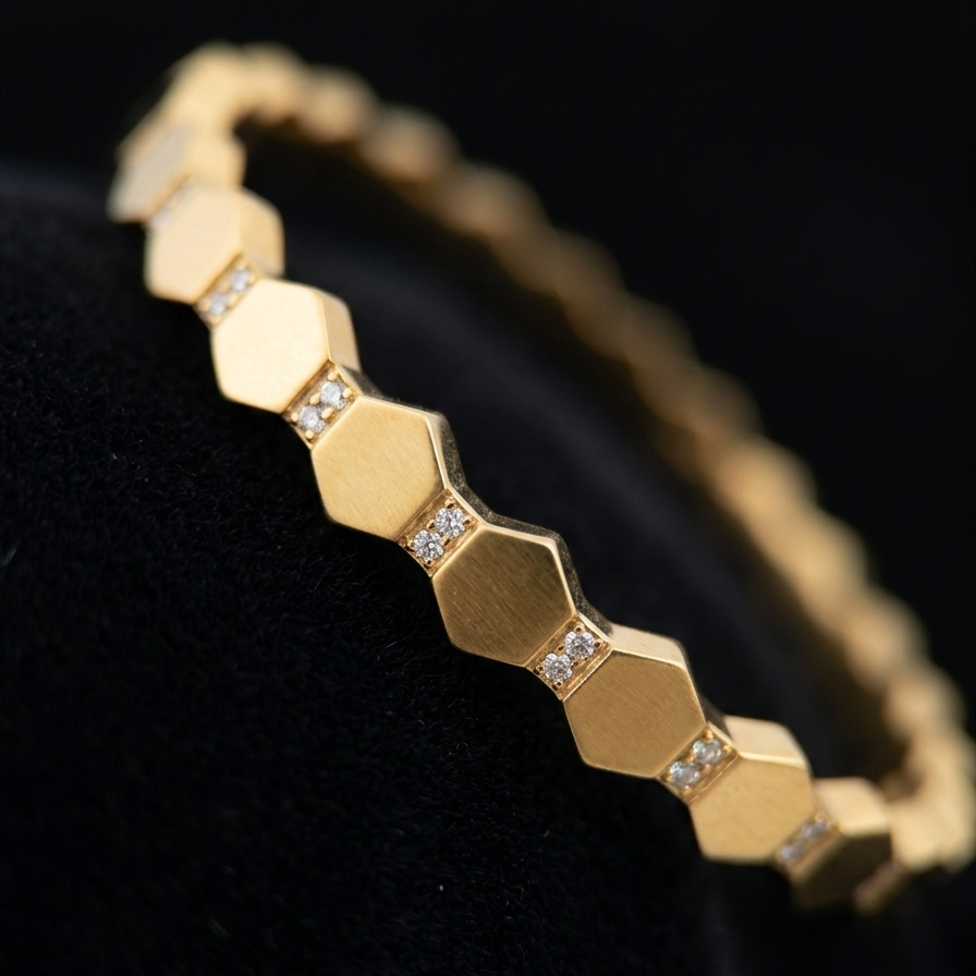 A gold hexagonal link bracelet with small clear stone accents, displayed on a black velvet jewelry stand against a dark background.