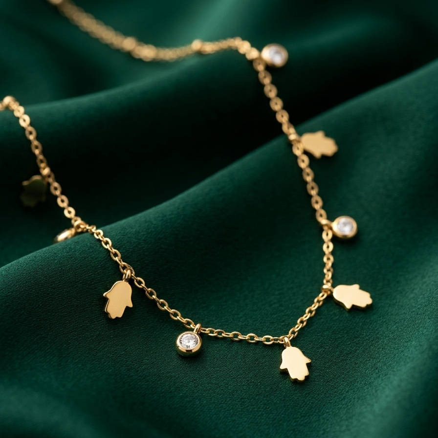 A delicate gold Hamsa hand necklace with small clear gemstone accents, displayed on draped dark green satin fabric.