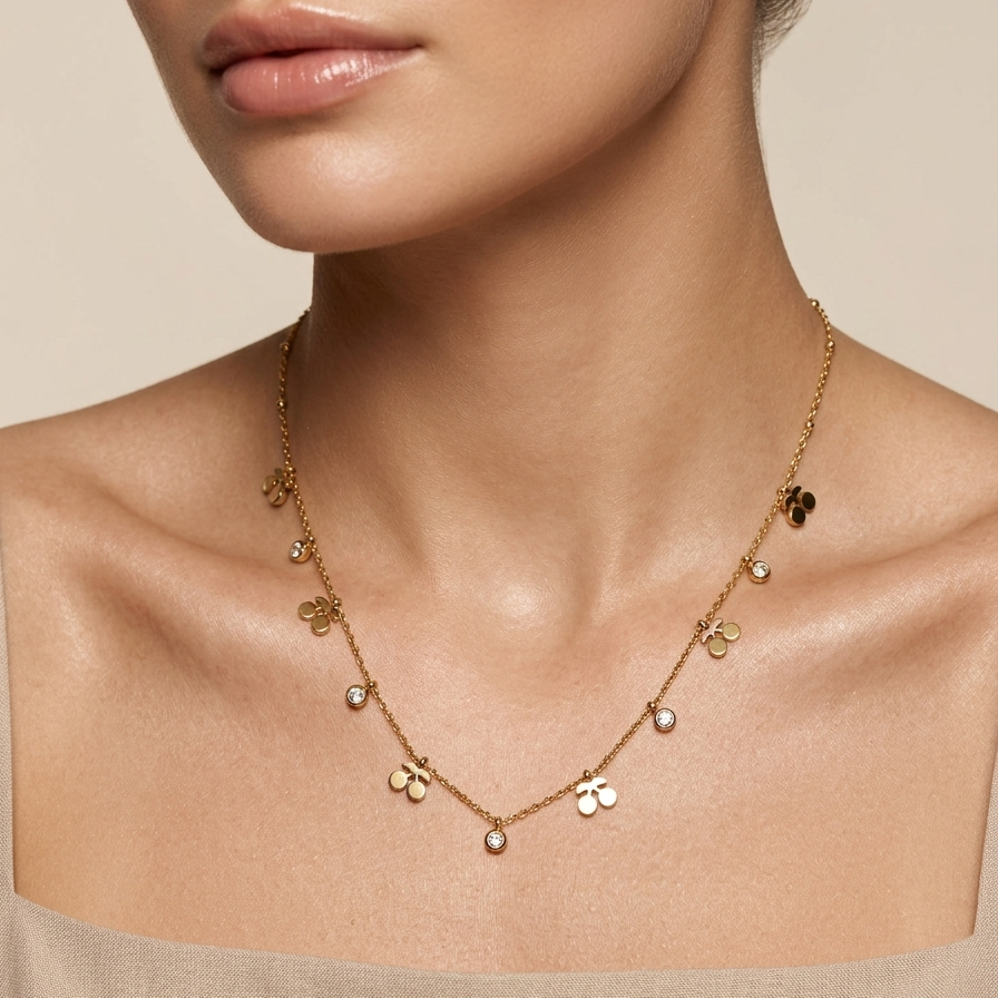 A close-up of a model wearing a delicate gold necklace with small clover and flower charms, paired with a beige off-the-shoulder top against a warm beige background.