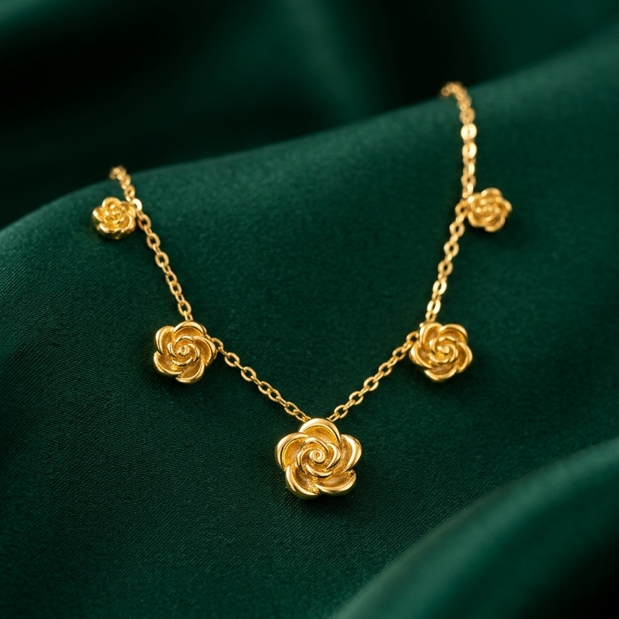 A gold necklace with five rose-shaped flower charms draped on a dark green satin fabric background.