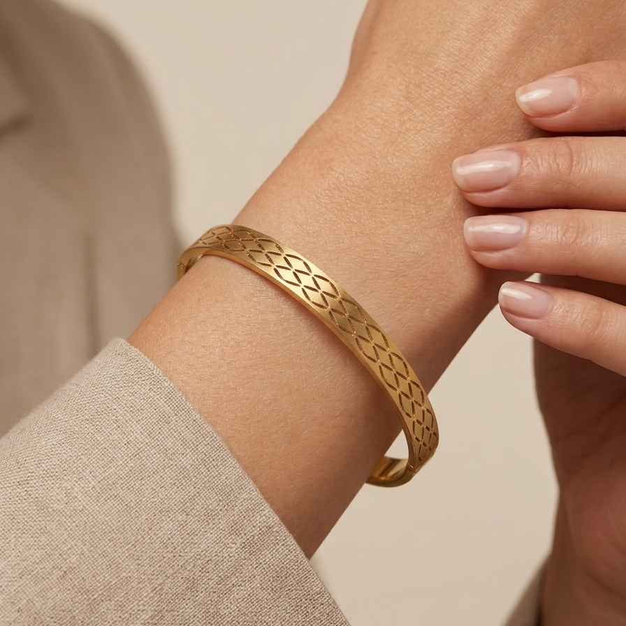 A close-up of a gold bangle bracelet with an intricate woven pattern, worn on a person's wrist.