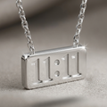 Close up of a Silver-tone rhodium plated necklace featuring a horizontal rectangular bar pendant engraved with the numbers 11:11.