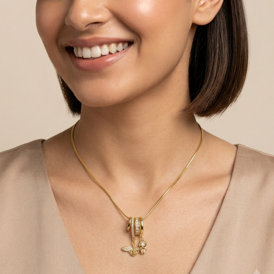 A close-up of a woman wearing a delicate gold chain necklace with a small anchor charm and pearl accents, set against a soft beige background.