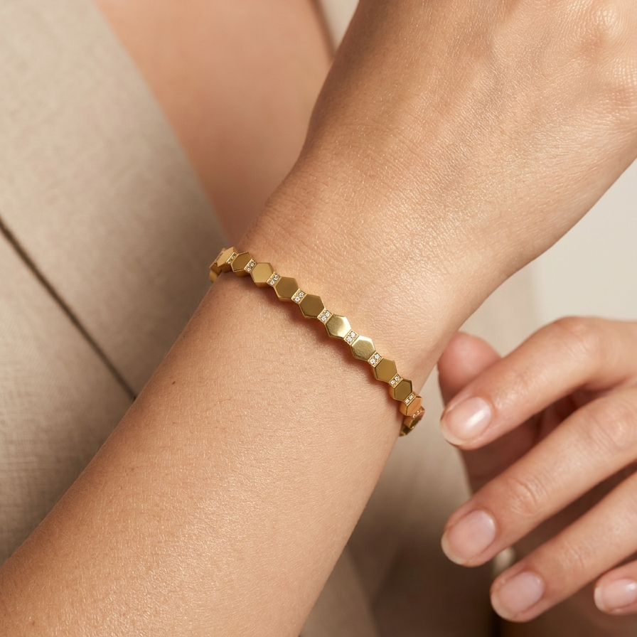 A close-up of a delicate gold bracelet with a repeating hexagonal link design, worn on a person's wrist.