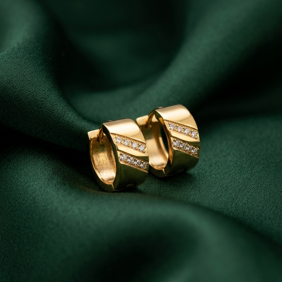 A pair of gold hoop earrings with a channel-set row of small clear stones, displayed on a draped dark green satin fabric.