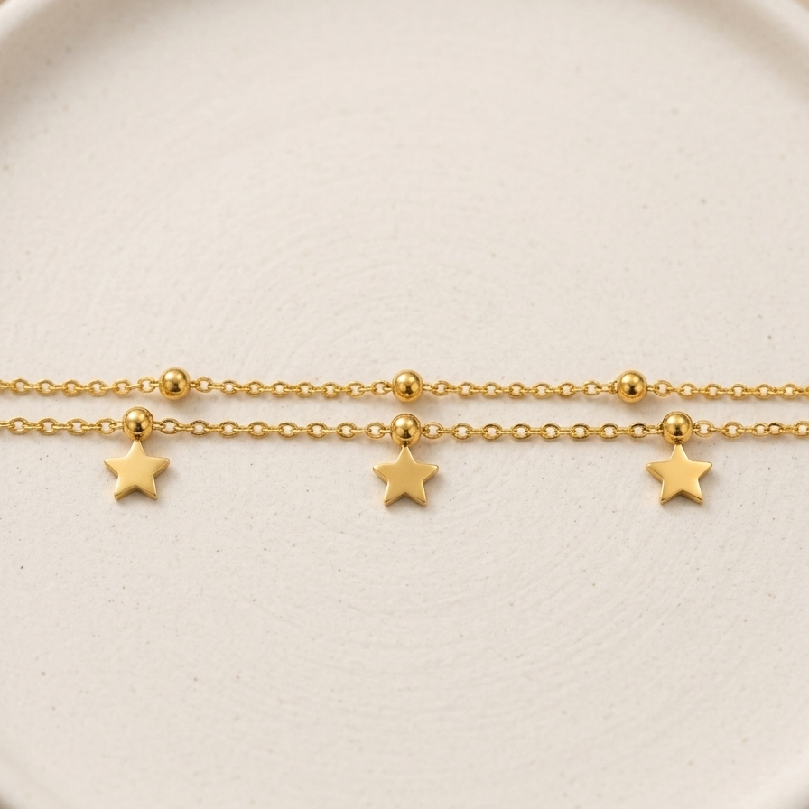A delicate gold chain bracelet featuring three small dangling star charms, displayed on a round, textured off-white ceramic plate.
