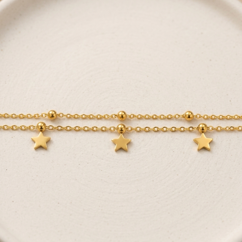 A delicate gold chain bracelet featuring three small dangling star charms, displayed on a round, textured off-white ceramic plate.