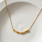 Gold necklace with curved bamboo texture bar sliding on a link chain on model neck.