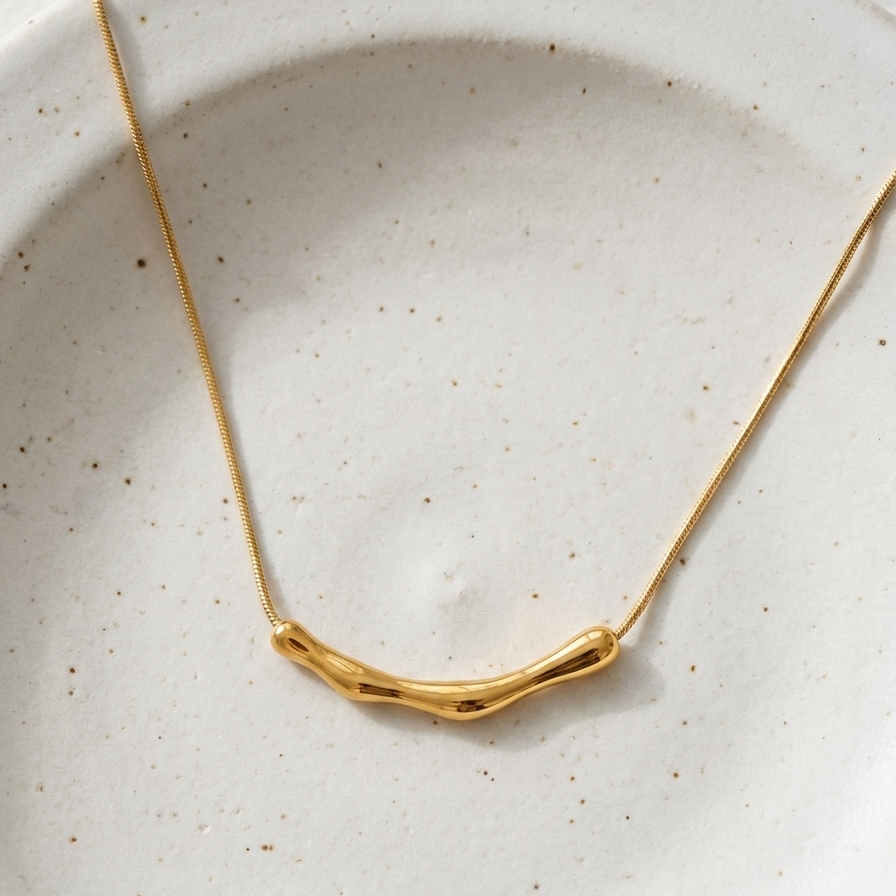 Gold necklace with curved bamboo texture bar sliding on a link chain on model neck.