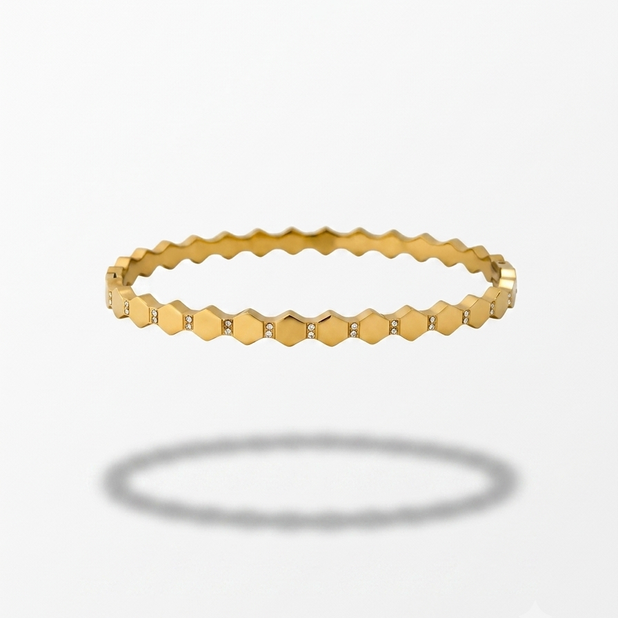 A gold bangle bracelet with a repeating hexagonal link pattern, shown floating against a light gray background with a soft shadow below.