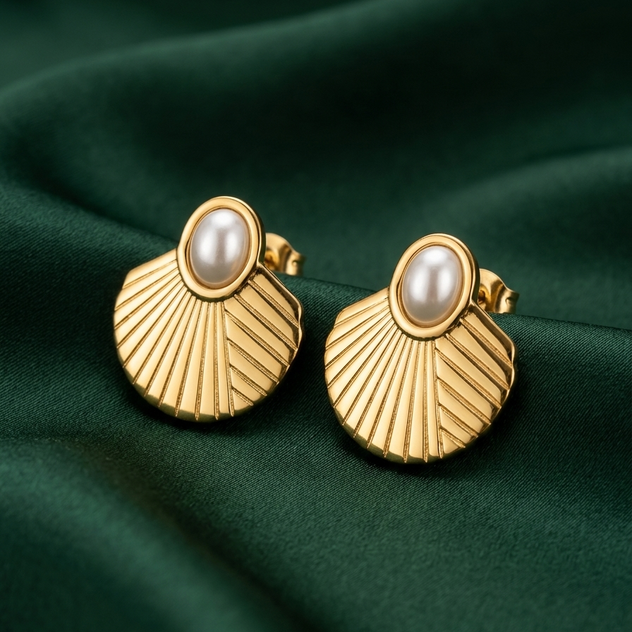 A pair of gold fan-shaped stud earrings with oval pearl centers, displayed on a dark green satin fabric background.