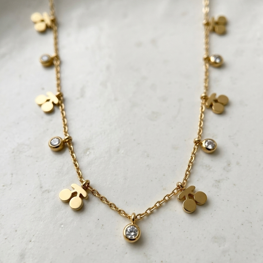 A delicate gold necklace featuring small gold charms, including three-leaf clovers, round discs, and bezel-set clear crystals, displayed on a light textured surface.