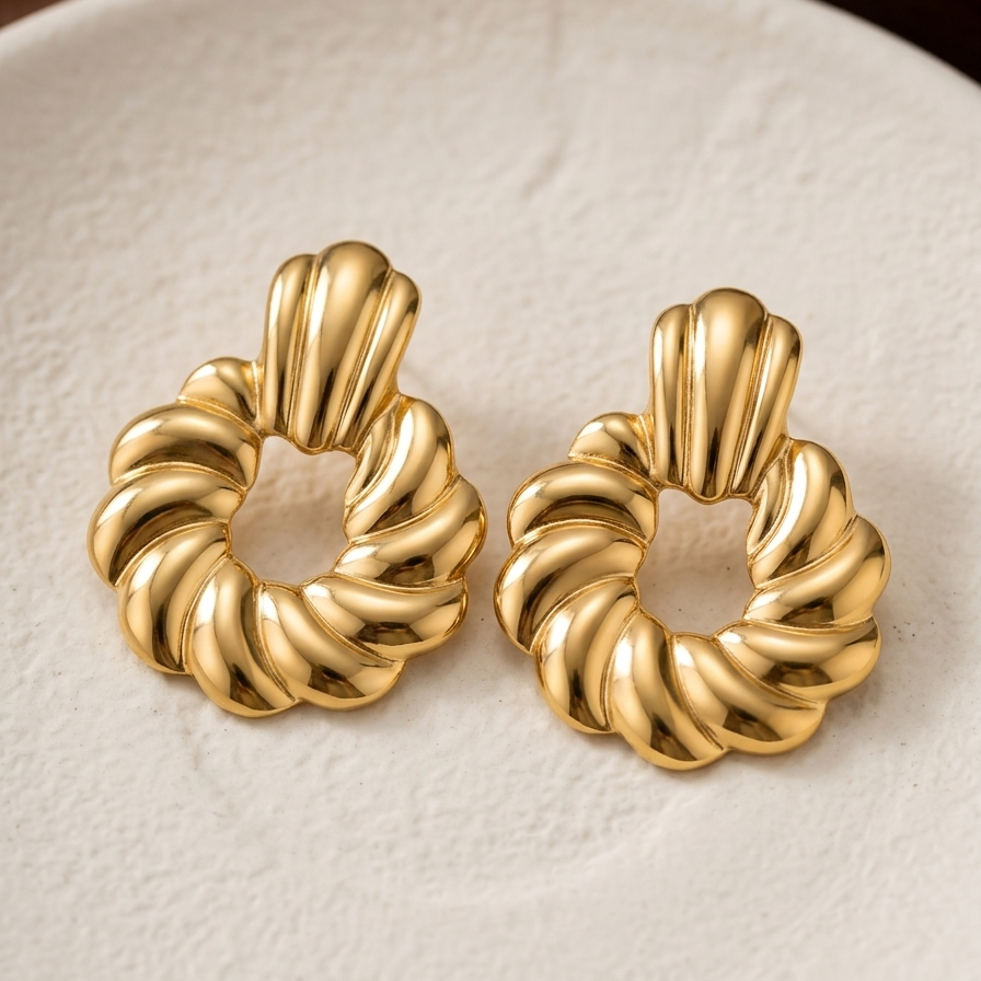 A pair of gold-toned twisted ring earrings with a textured, ribbed design, displayed on a light beige textured surface.