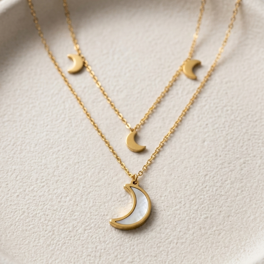 A delicate gold necklace with three crescent moon pendants in varying sizes, displayed on a textured cream-colored jewelry stand.