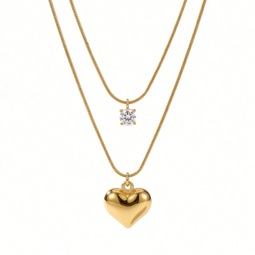 Double layered 18kt gold plated necklace with crystal solitaire and puffy heart pendant floating on white background.