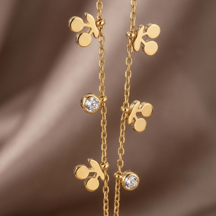 A close-up of a gold-toned necklace with repeating clover-like motifs and small clear gemstone accents, photographed against a soft brown satin-like background.