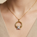 A gold necklace with a circular pendant and a silver-toned cross detail set with small clear stones, shown worn on a model's neck.